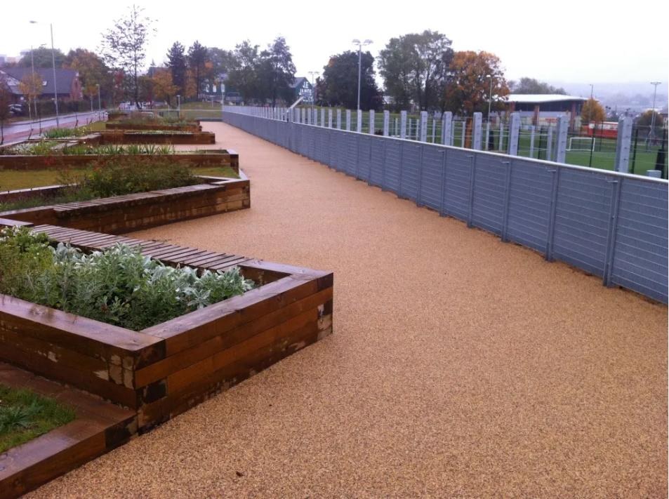 Raised terrace with timber planters and a galvanised mesh and wire rope balustrade overlooking a floodlit 3G football pitch in Sheffield